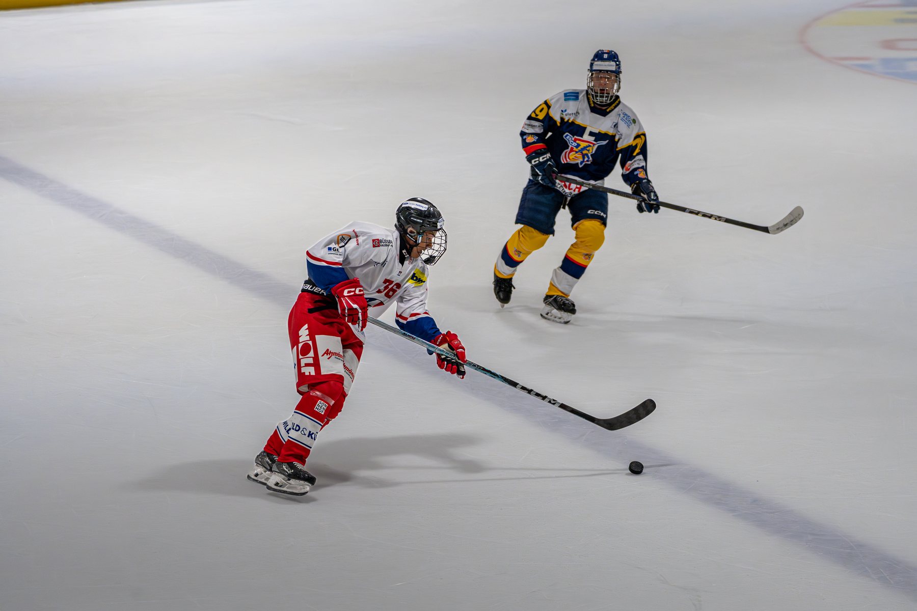 Rapperswiler Spieler spielt den Puck, Dübendorfer Gegenspieler läuft an