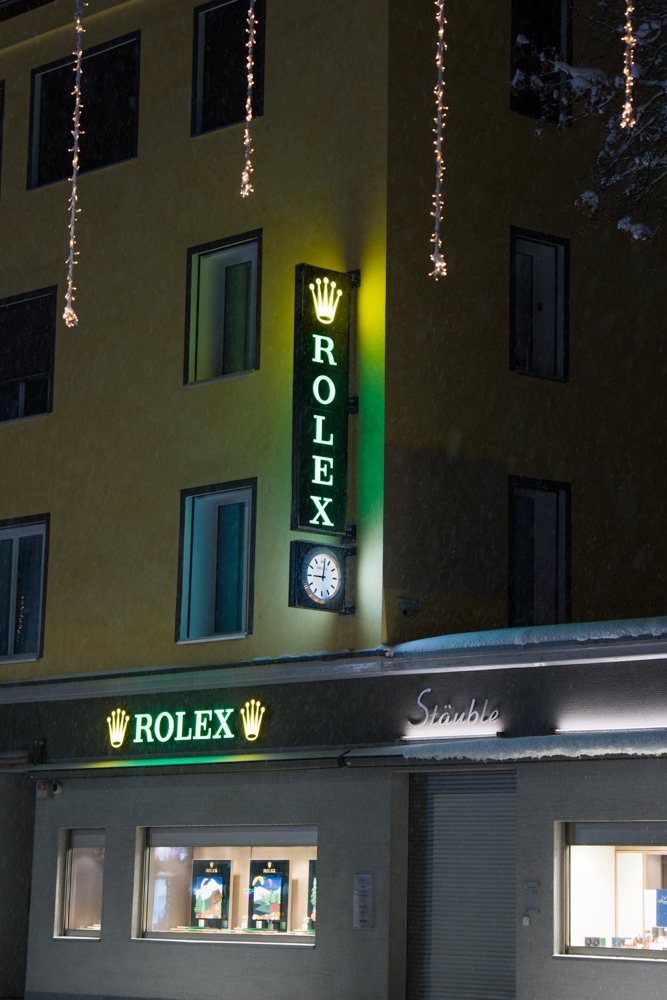 Leuchtschrift eines Uhrengeschäfts an verschneiter Fassade, Davos